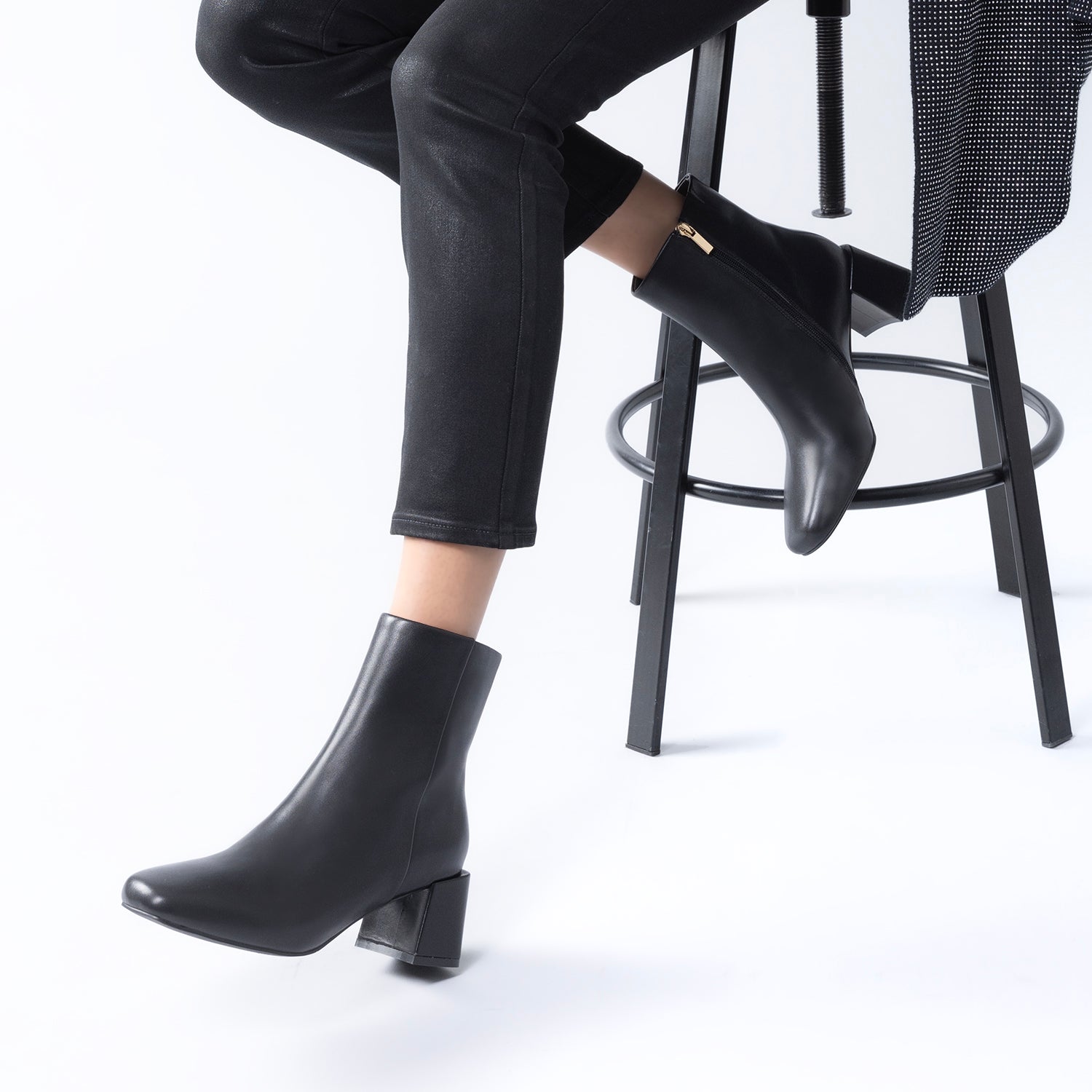 A person seated with black ankle boots with a block heel, square toe, and chiselled silhouette.