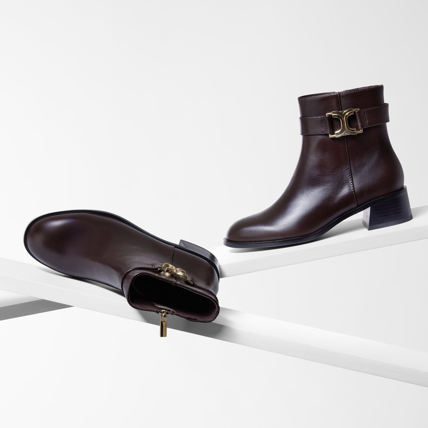 Pair of brown leather ankle boots with gold buckles on a white background