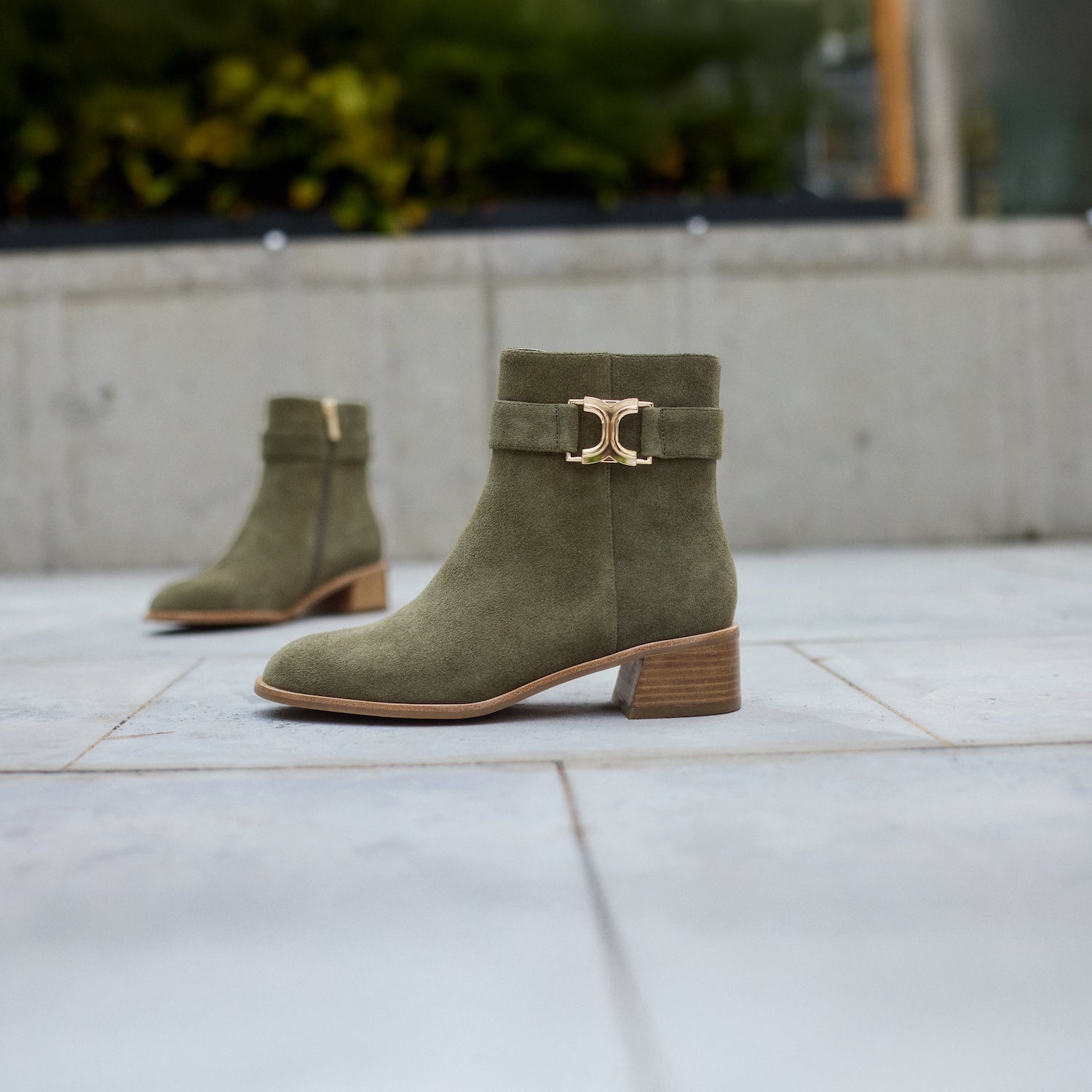 Green suede boots with gold buckle on a tiled floor