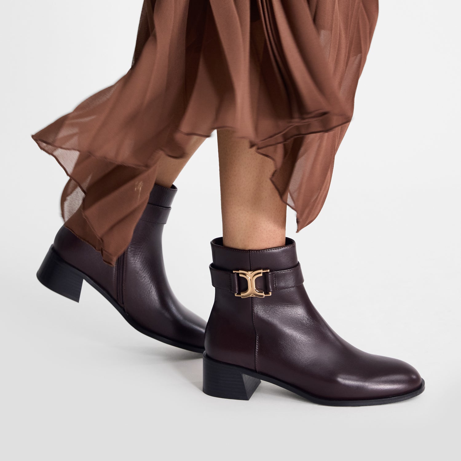 Brown ankle boots with a gold buckle worn by model on a white background