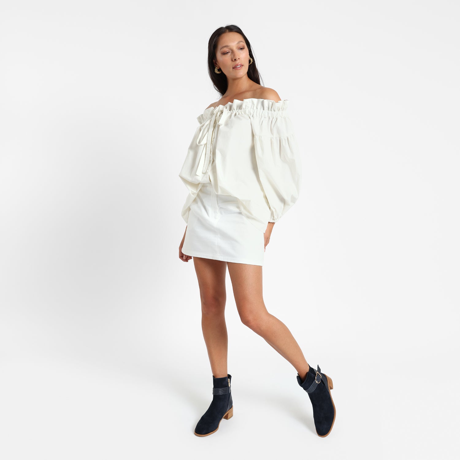 Bologna navy suede ankle boot on model wearing a white mini skirt and a puffy blouse.