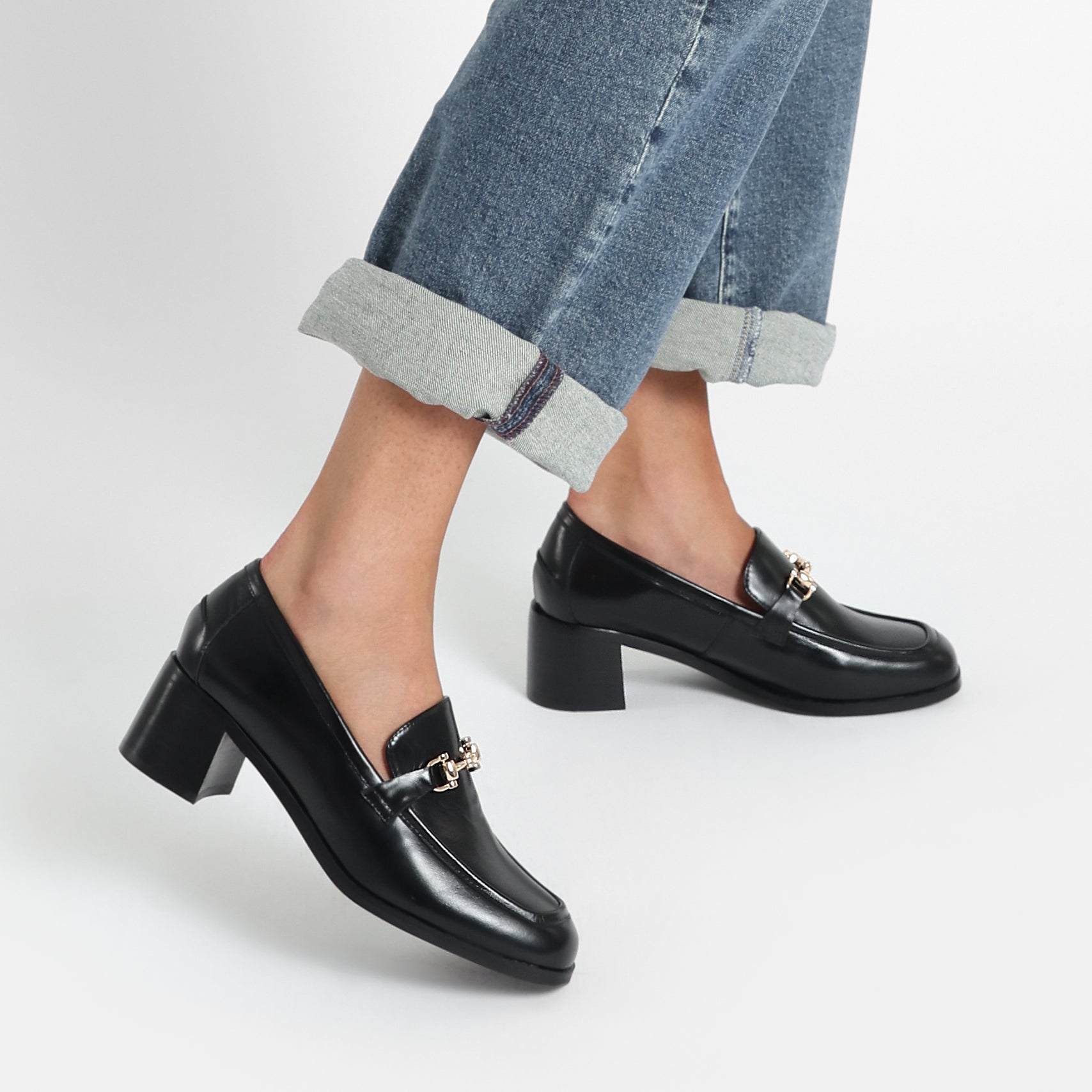 Woman wears Bremen Loafer in black with block heel of 4.5cm. Gold buckle.