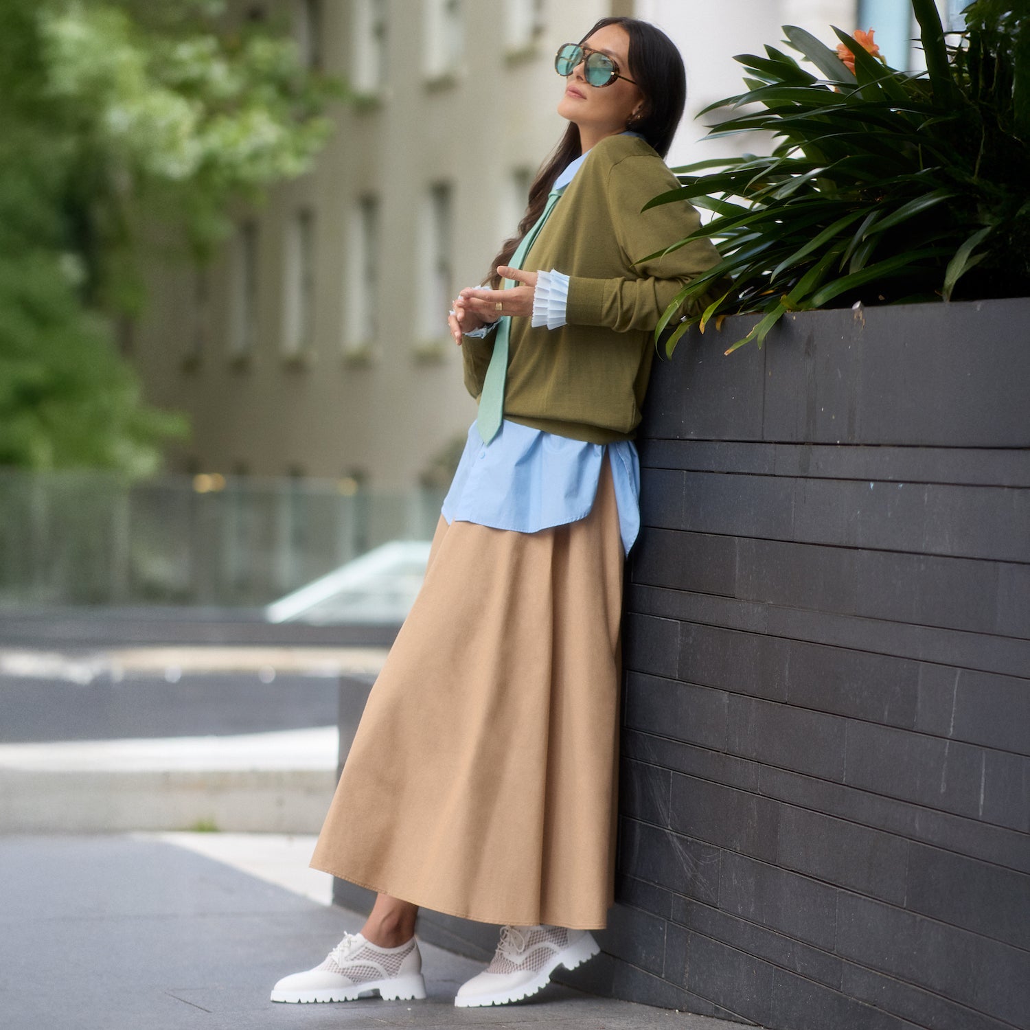 Woman in stylish outfit wearing Cassidy flats in white leaning against a wall outdoors.
