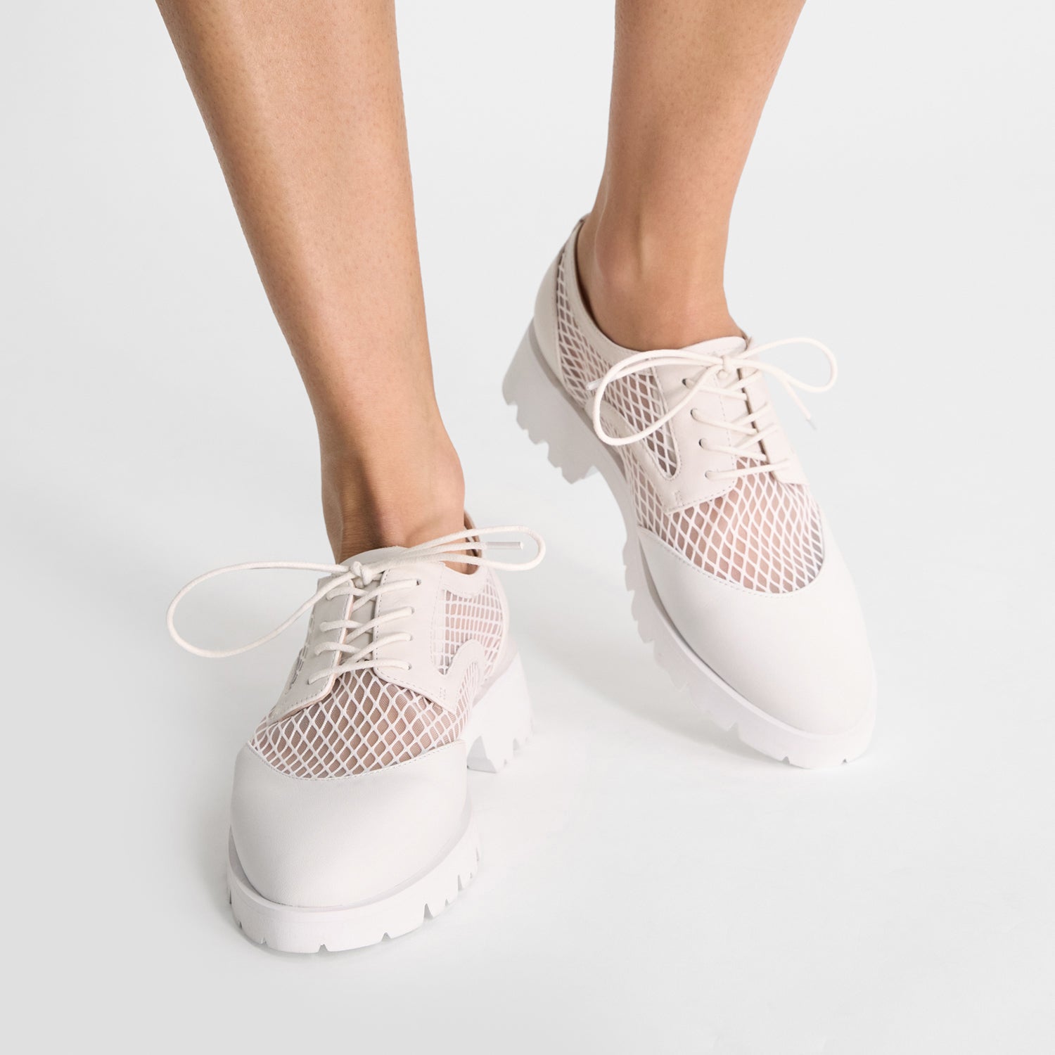 White Cassidy flats with mesh panels worn by a person on a light gray background