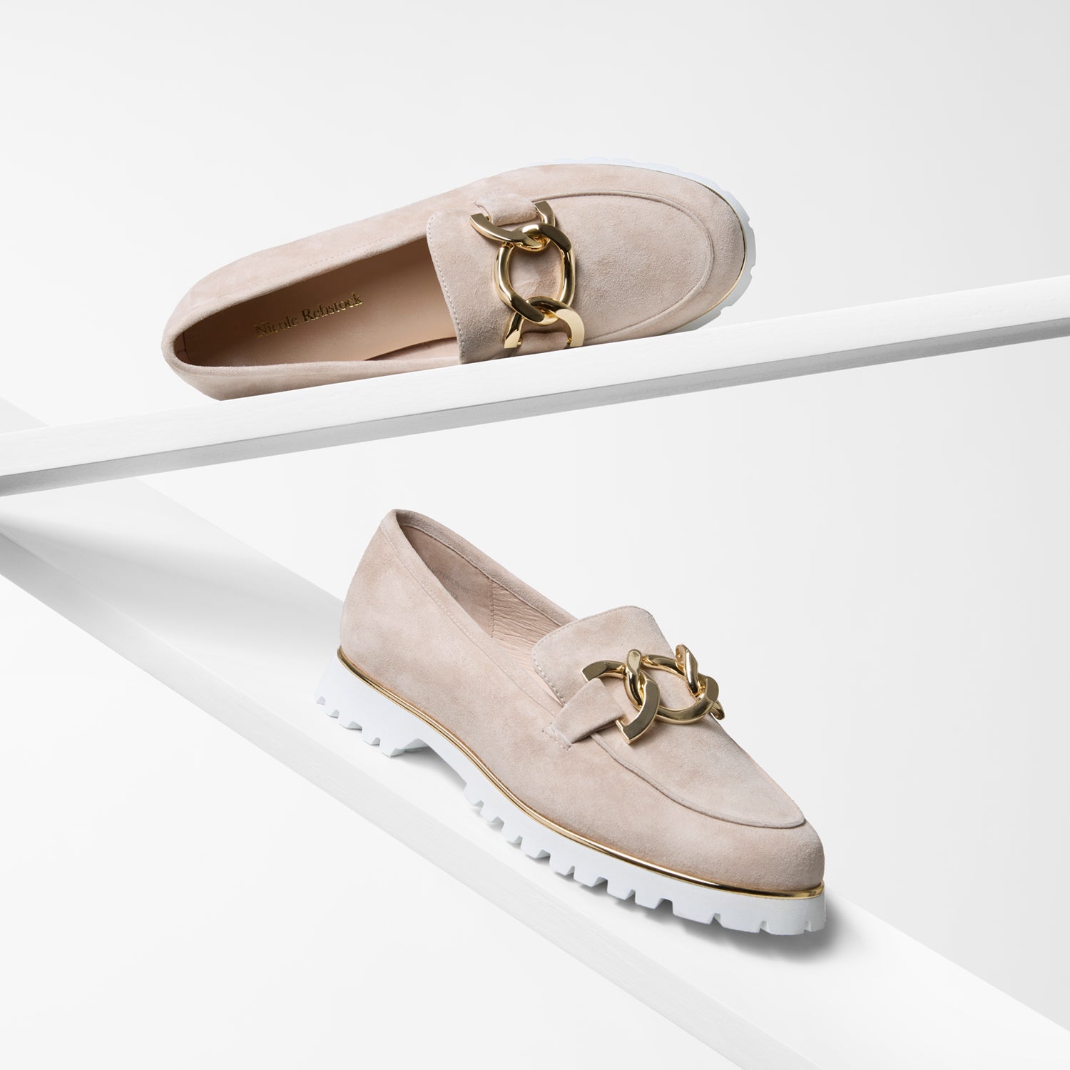 Nude suede loafers with gold accents on a white background