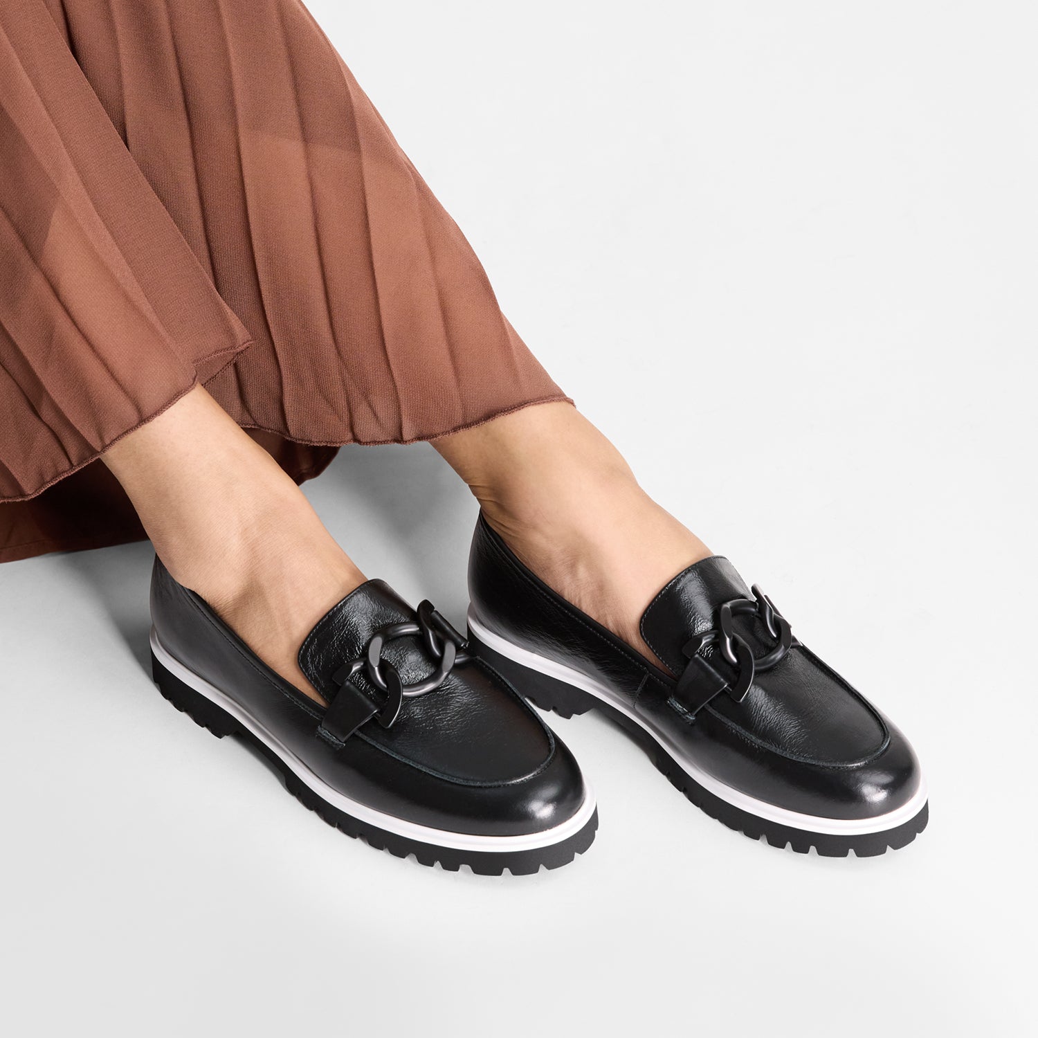 Black leather loafers with black buckle shown up close on models feet.