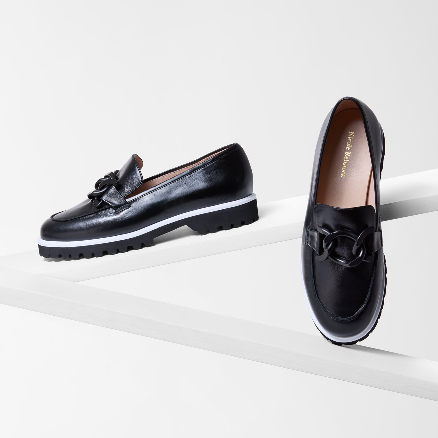 Flat black loafers with a black metal buckle and contrasting white trim shown from various angles.