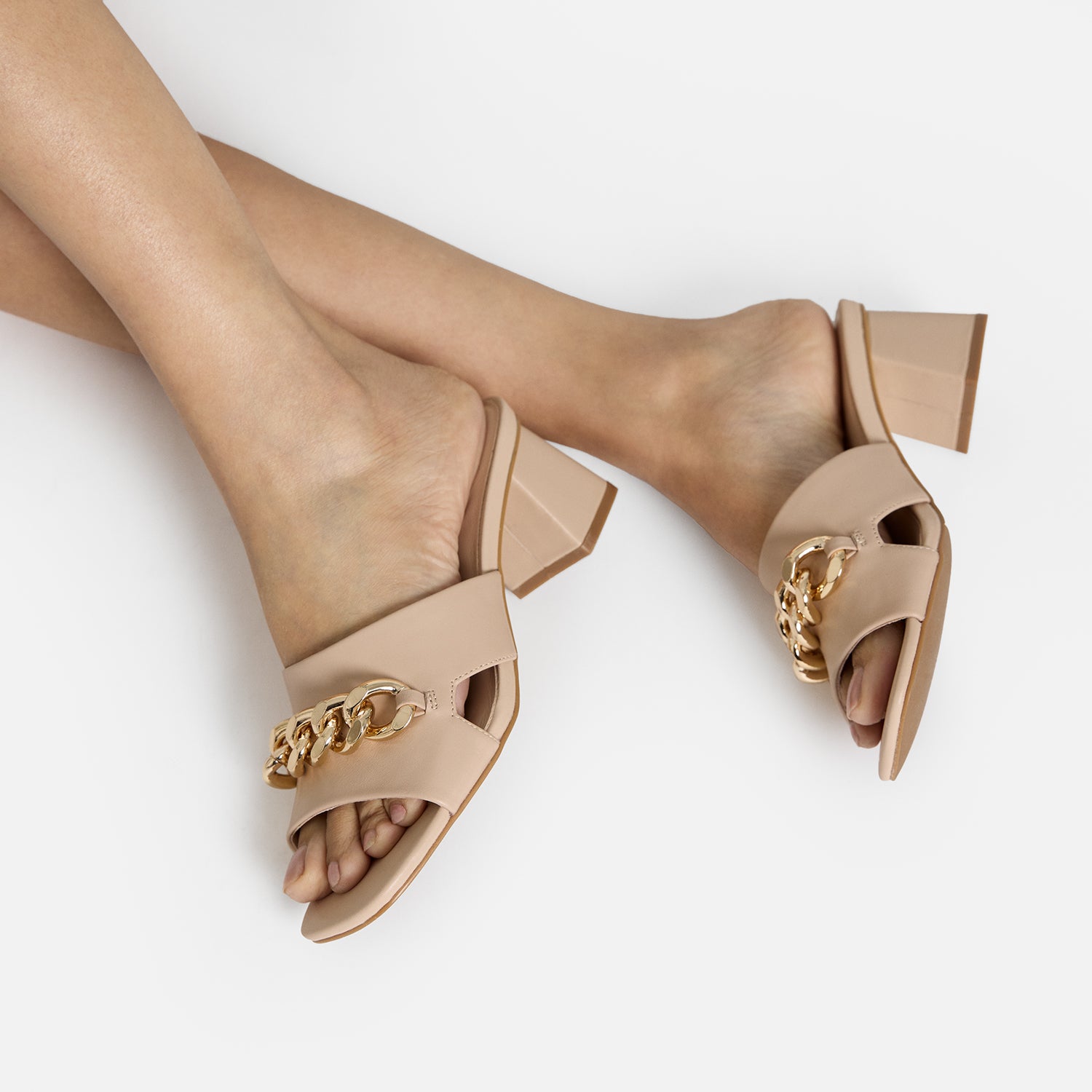 Close up of nude sandal called Evie shown on woman’s feet. Metal gold chain details.