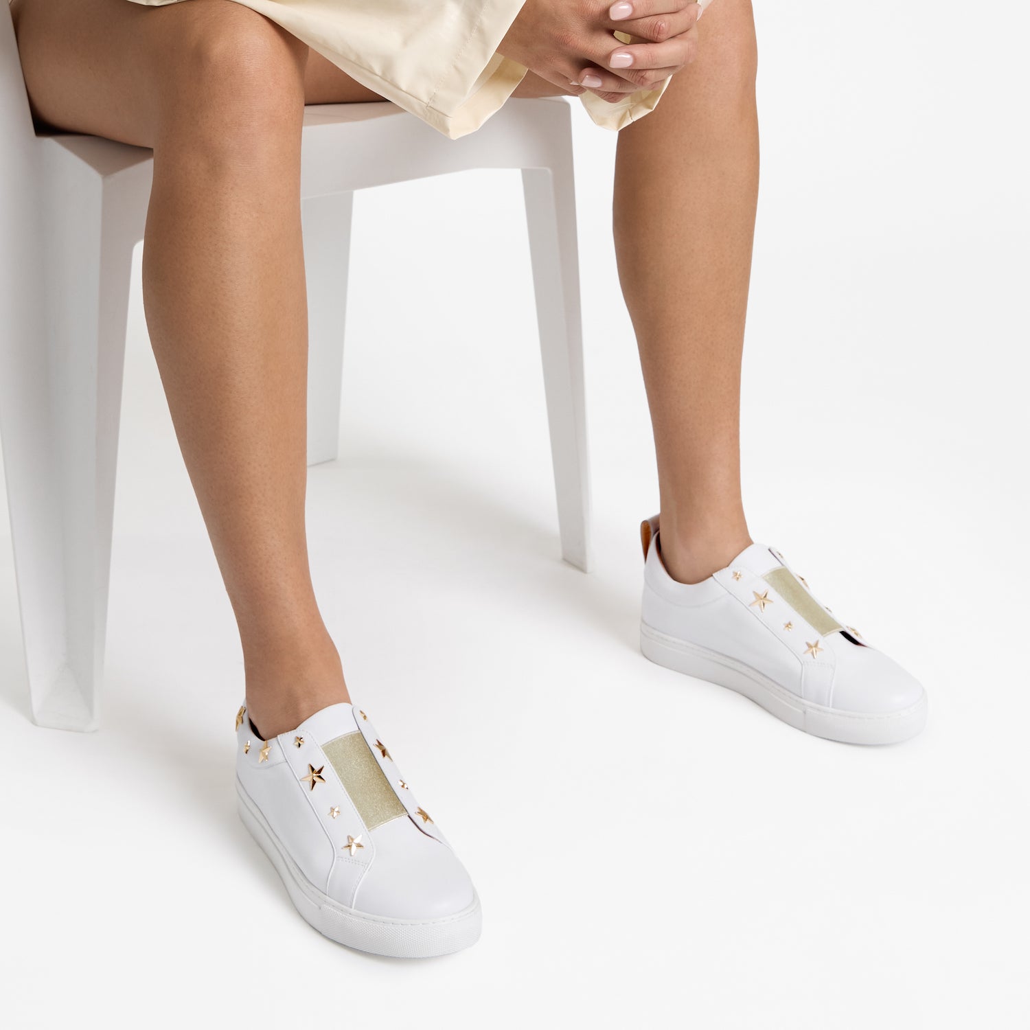 Close up on model of white pull on sneakers with gold star studs