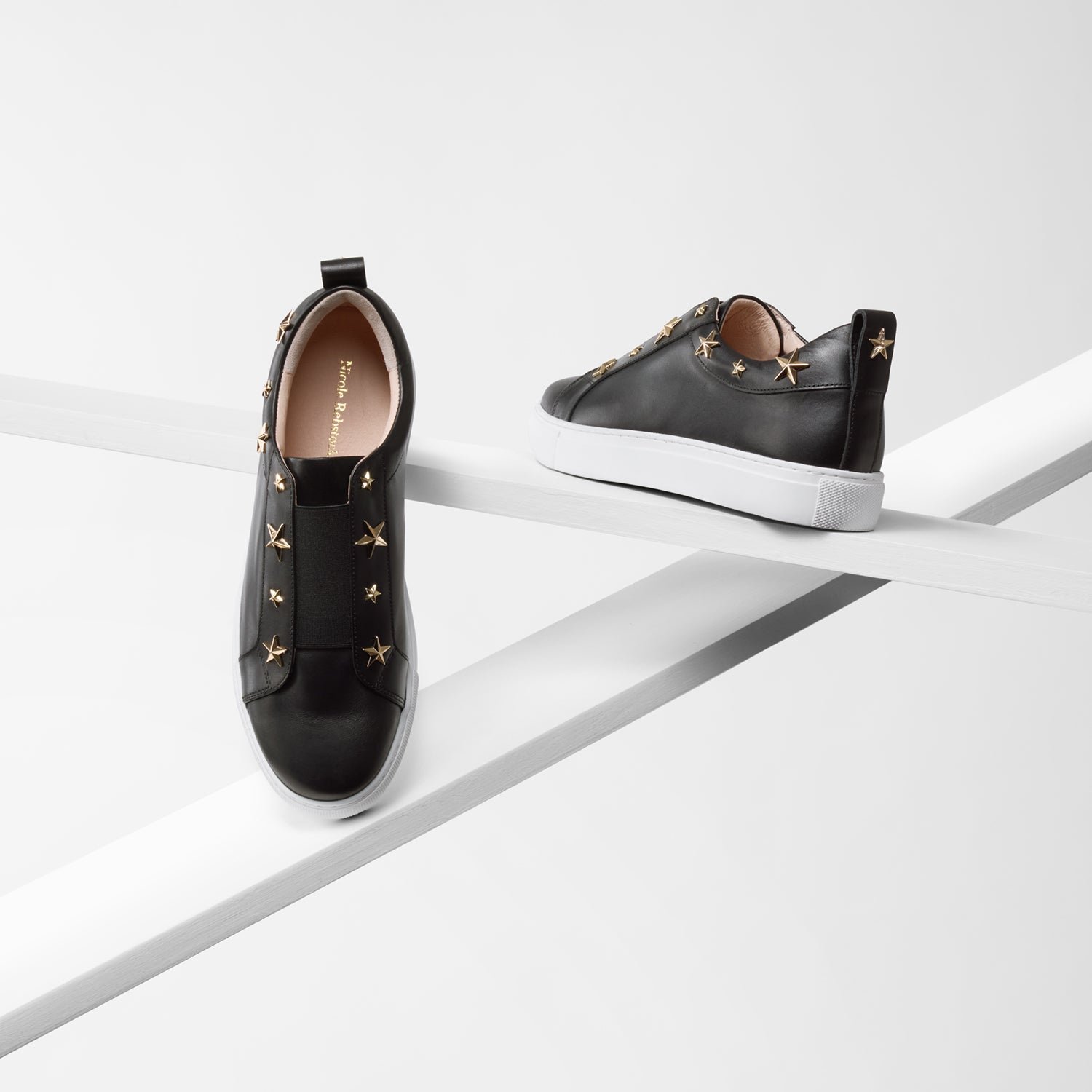 Felix black leather pull on sneaker on planks showing all angles. Gold stars and black elastic detailing with white sole.
