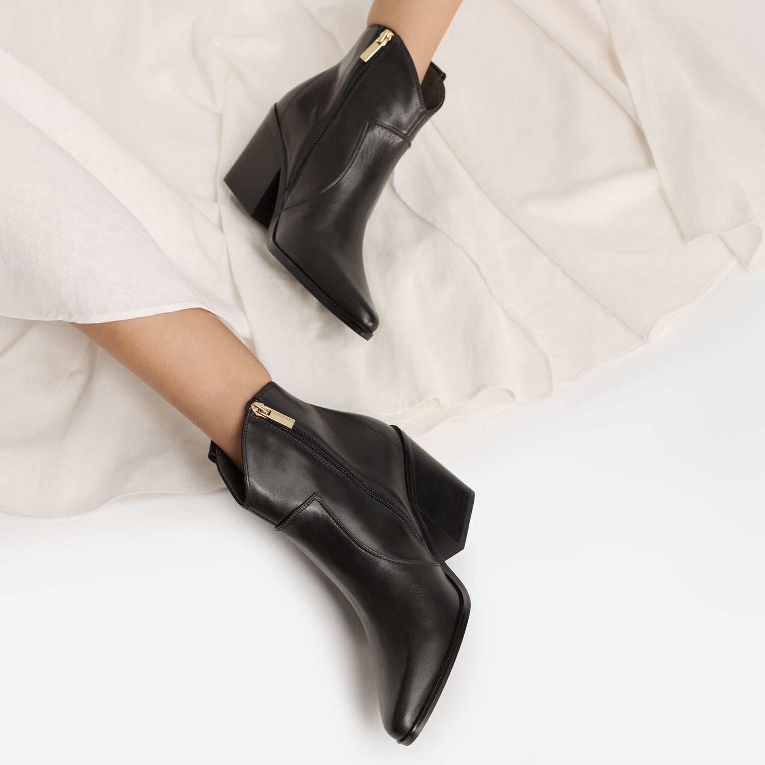 Black cowboy boots worn by model with almond toe and stitching detailing.