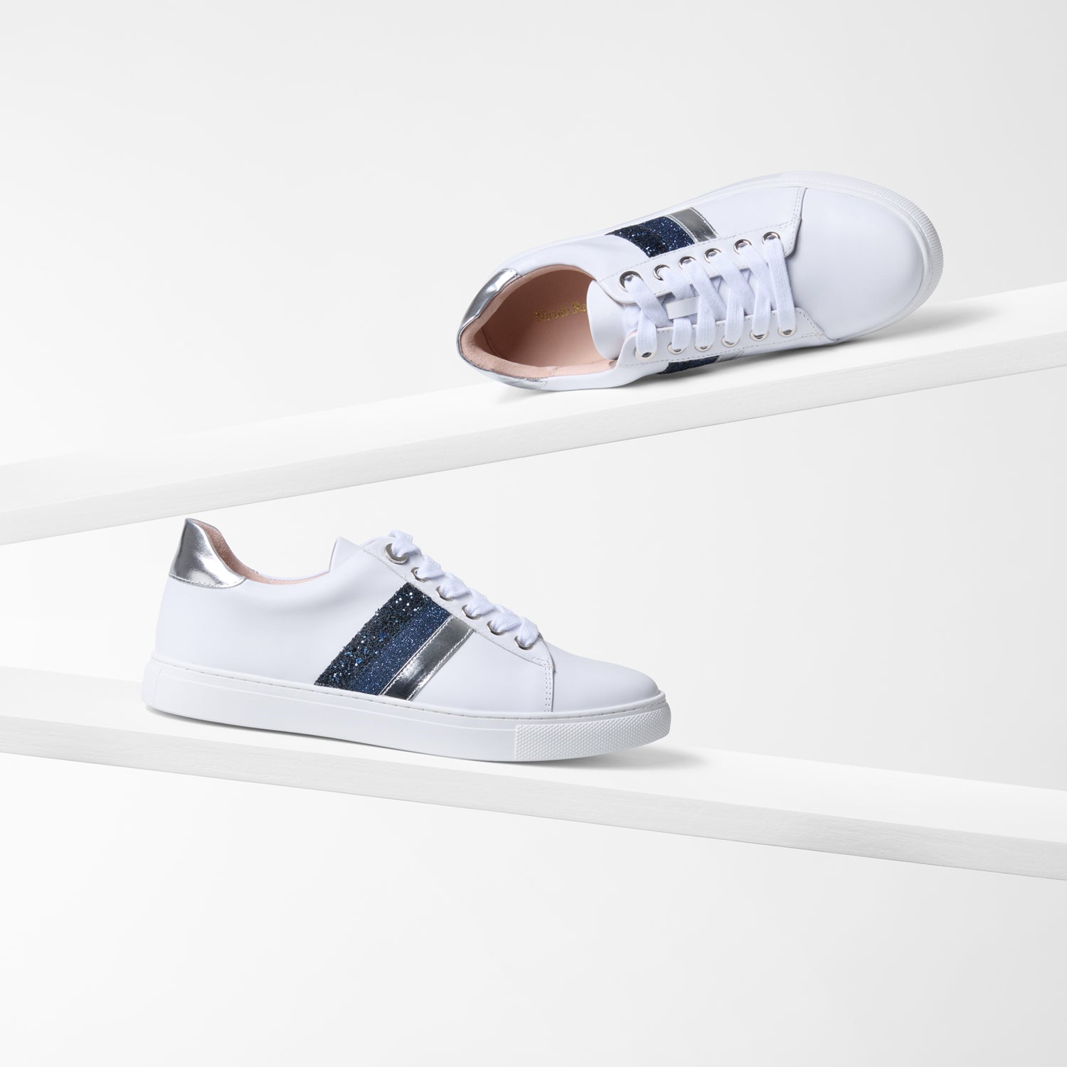 White Gigi Sneakers with silver and blue accents on a light background by Nicole Rebstock