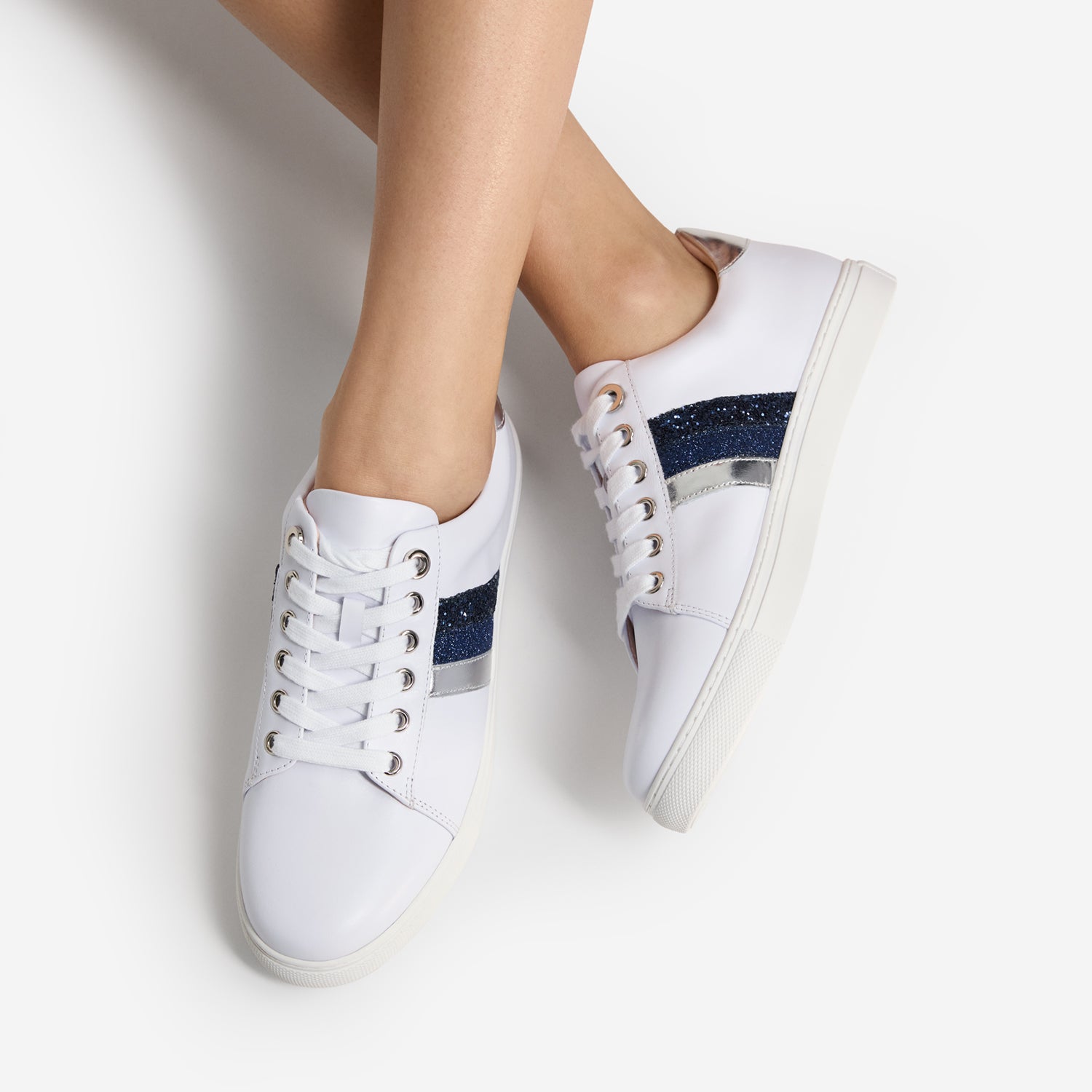 White sneakers with blue and silver stripes and laces worn by a person on a light gray background