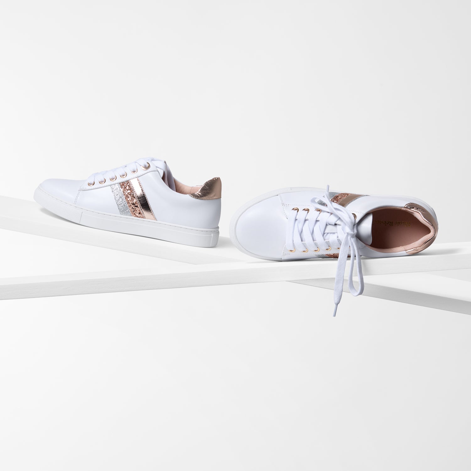 White leather sneakers with rose gold accents on a white background with white laces.