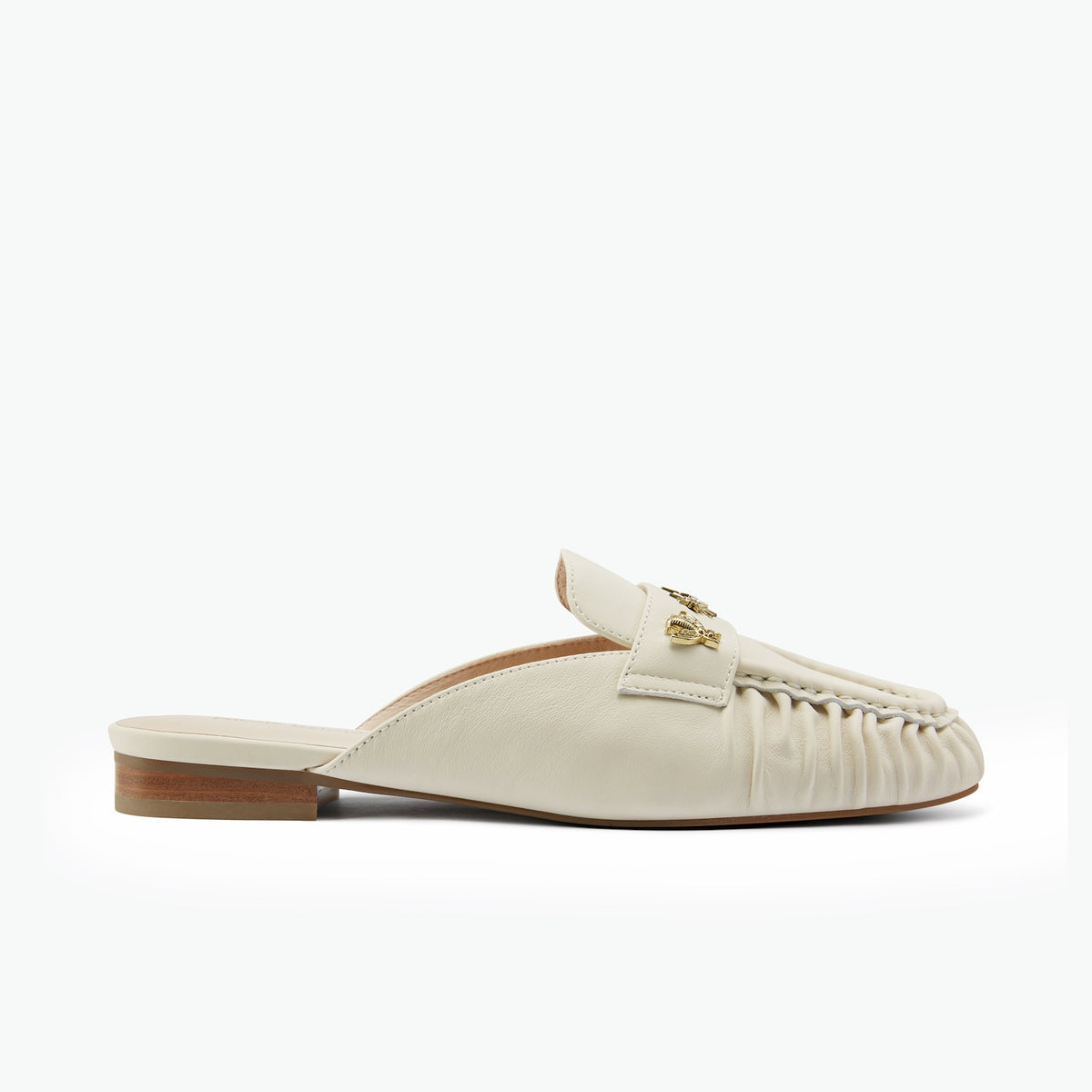 An off-white leather mule loafer with a gold stud detail on the strap, a ruched toe, and a low stacked wood-look heel, shown in profile against a white background.