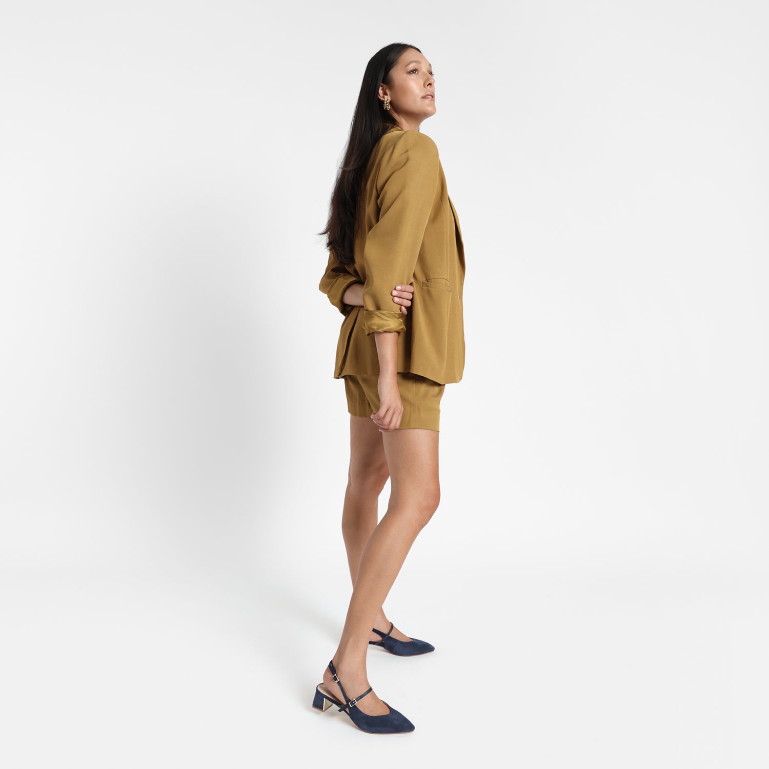 Woman wears Harper Slingback shoe in navy suede. Shoes feature a Mary Jane Strap and block heel with gold buckle and internal heel detailing.