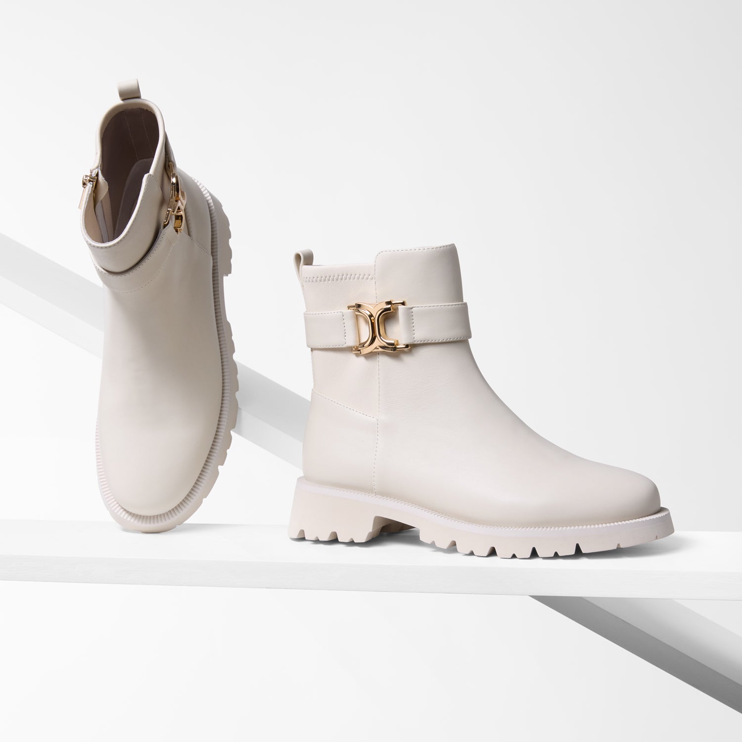 Pair of ivory thick thread boots with gold buckles on a light grey background