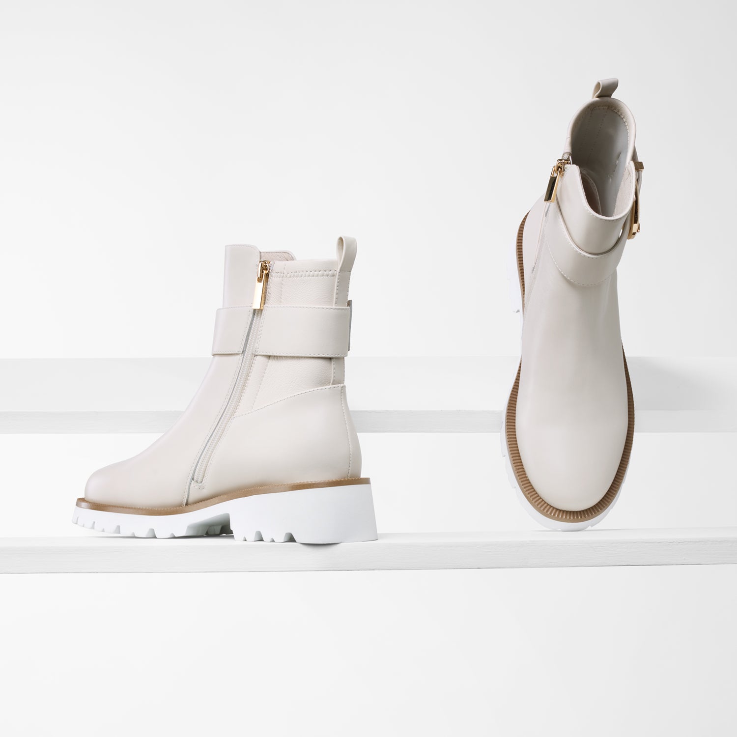 Jaxon ivory leather ankle boot on planks showing rounded toe, tan trim and strap with gold buckle.