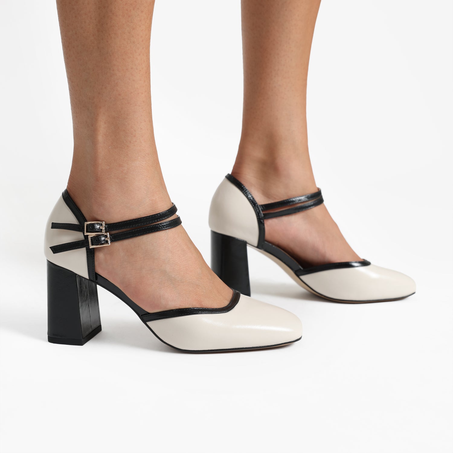Close up of ivory and black pumps called Jelico with two slim Mary Jane straps and a square toe.