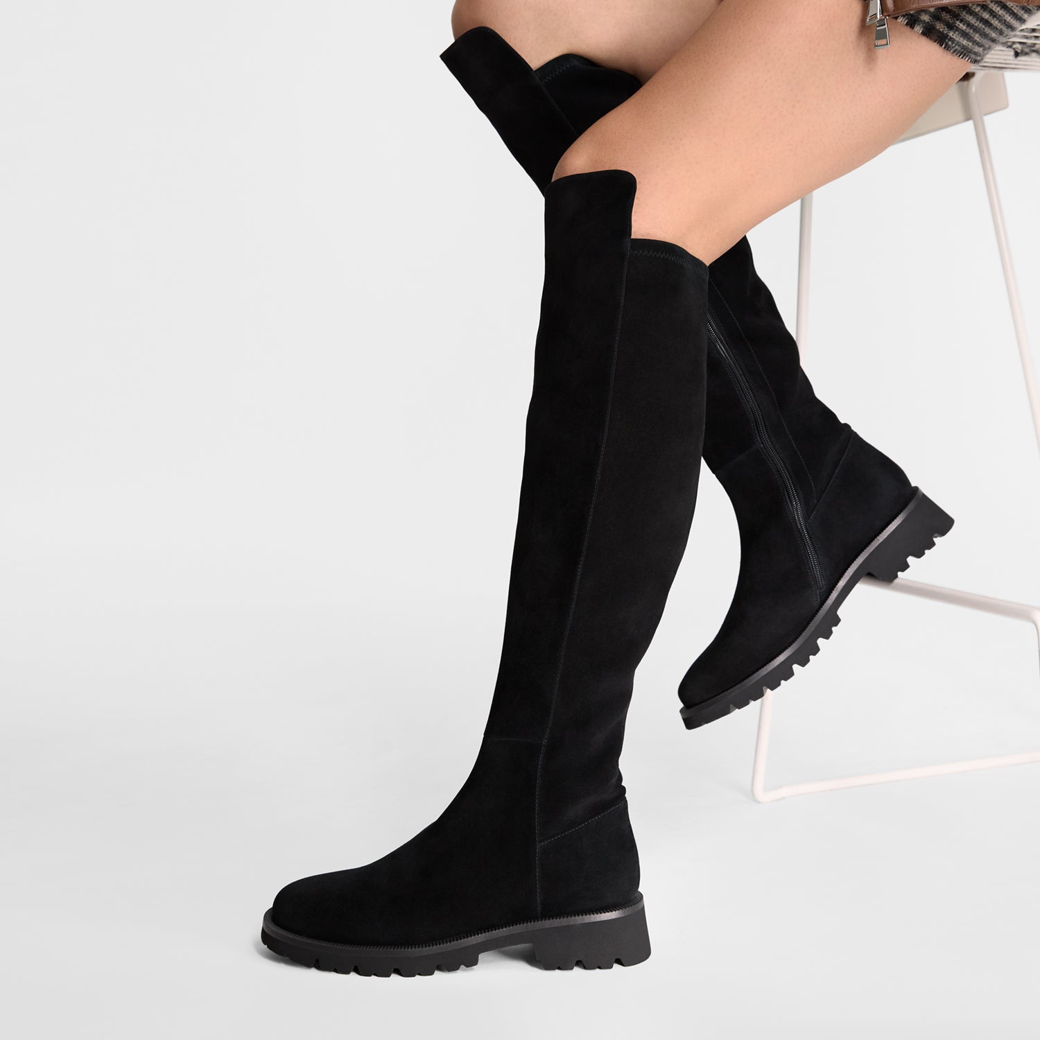 Black knee-high boots worn by a person on a white background. Round toe and tread sole.