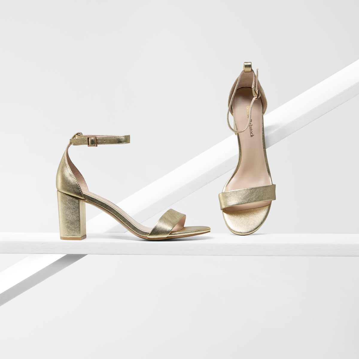 A pair of metallic gold block-heel sandals with ankle straps, shown from side and top views on a clean white geometric studio background.