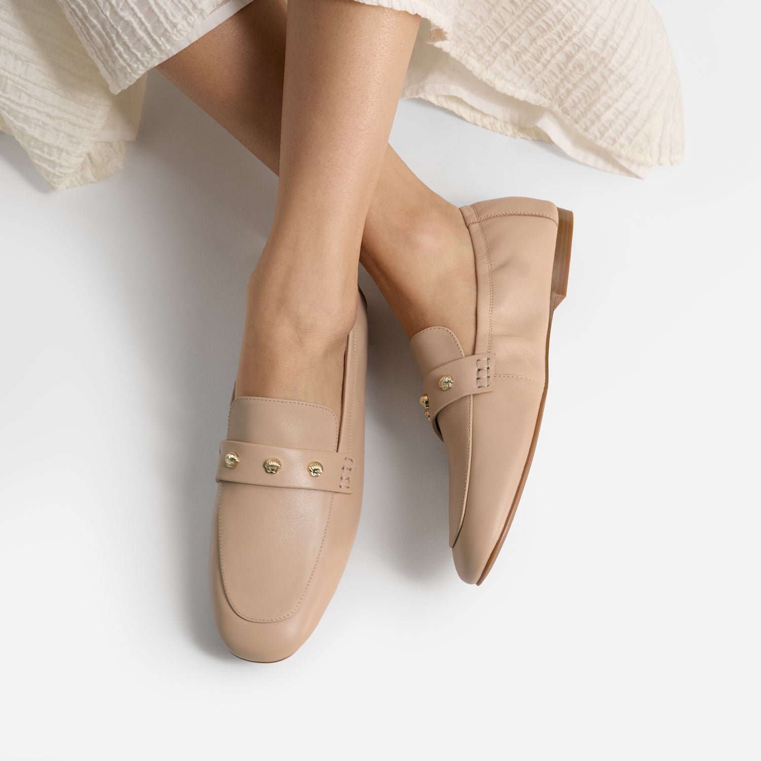 Nude loafers worn with a light-colored skirt on a white background by Nicole Rebstock