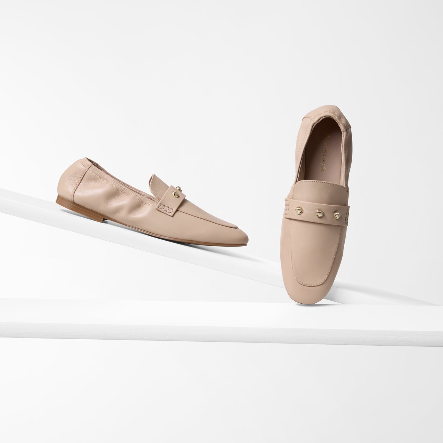 Pair of light tan loafers on a white background with almond toe and gold details.