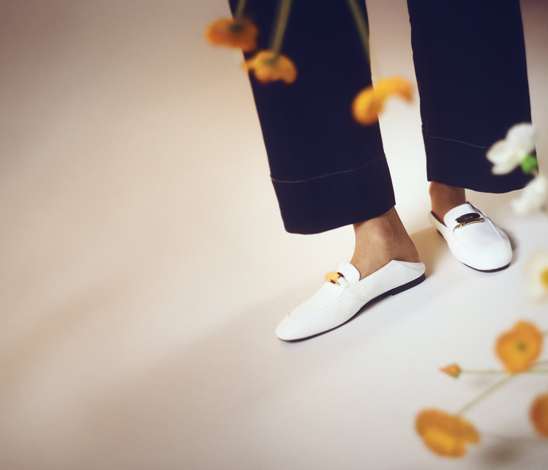White loafers worn with navy pants on a neutral background