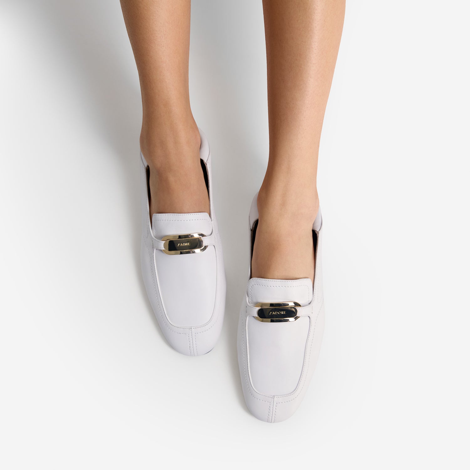 White loafers with gold accents worn by a person on a white background