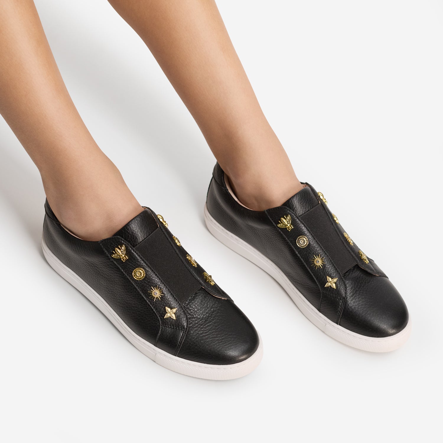 A pair of black leather slip-on sneakers with gold-tone decorative studs and star motifs, worn by a model against a clean white background.