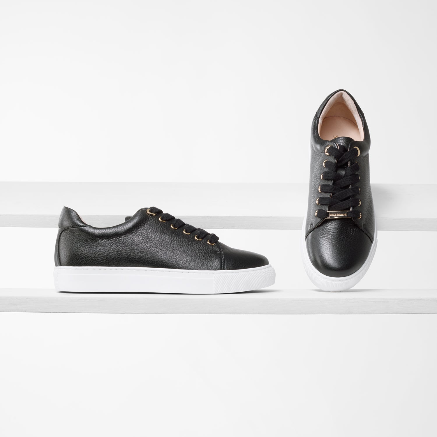 Mace black leather pebble trainer on planks highlighting gold detail on laces.