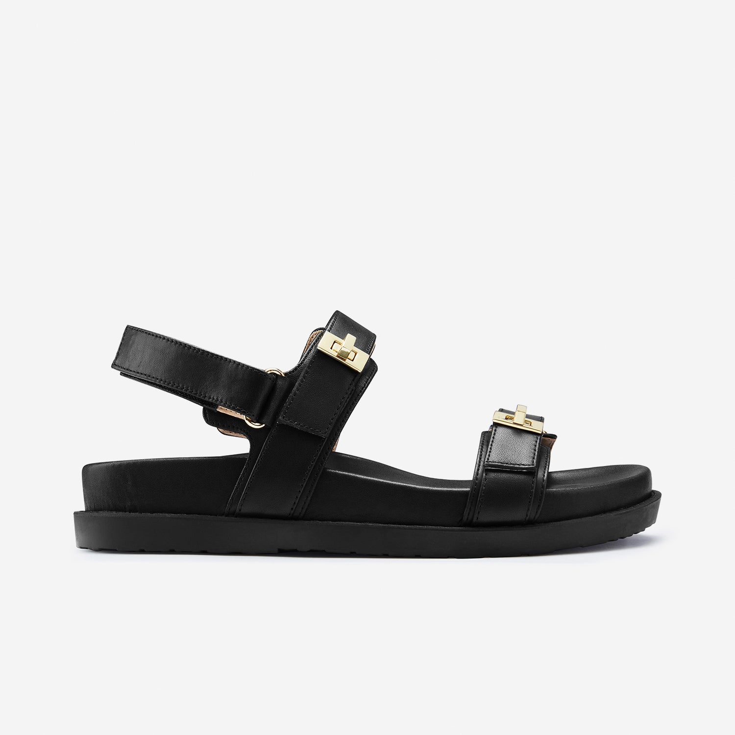 Side profile of the Maine flat sandal I’m black. Velcro strap with gold highlights.
