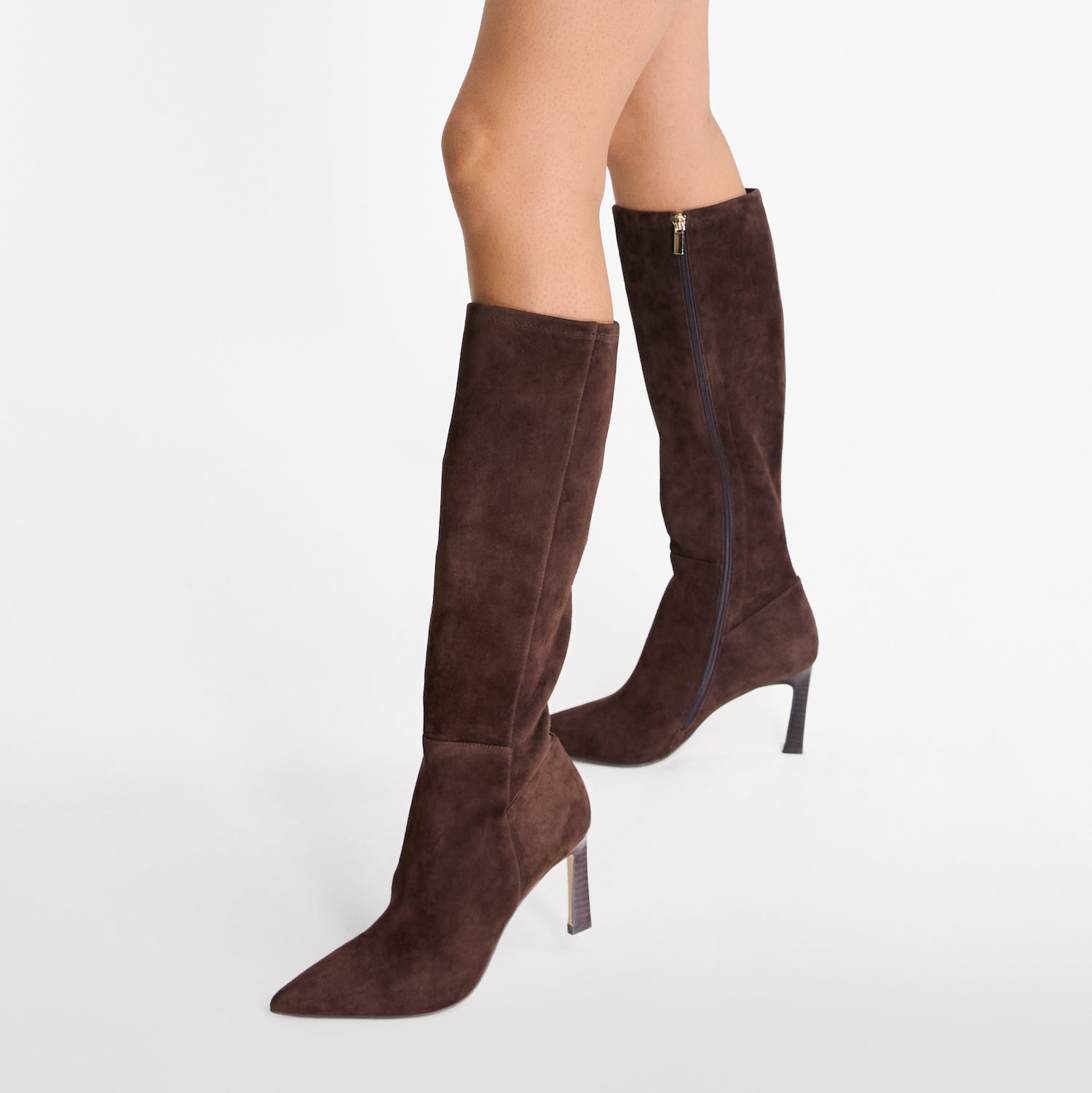 Brown suede knee-high boots on a white background worn by model. Pointed toe and 8cm heel.