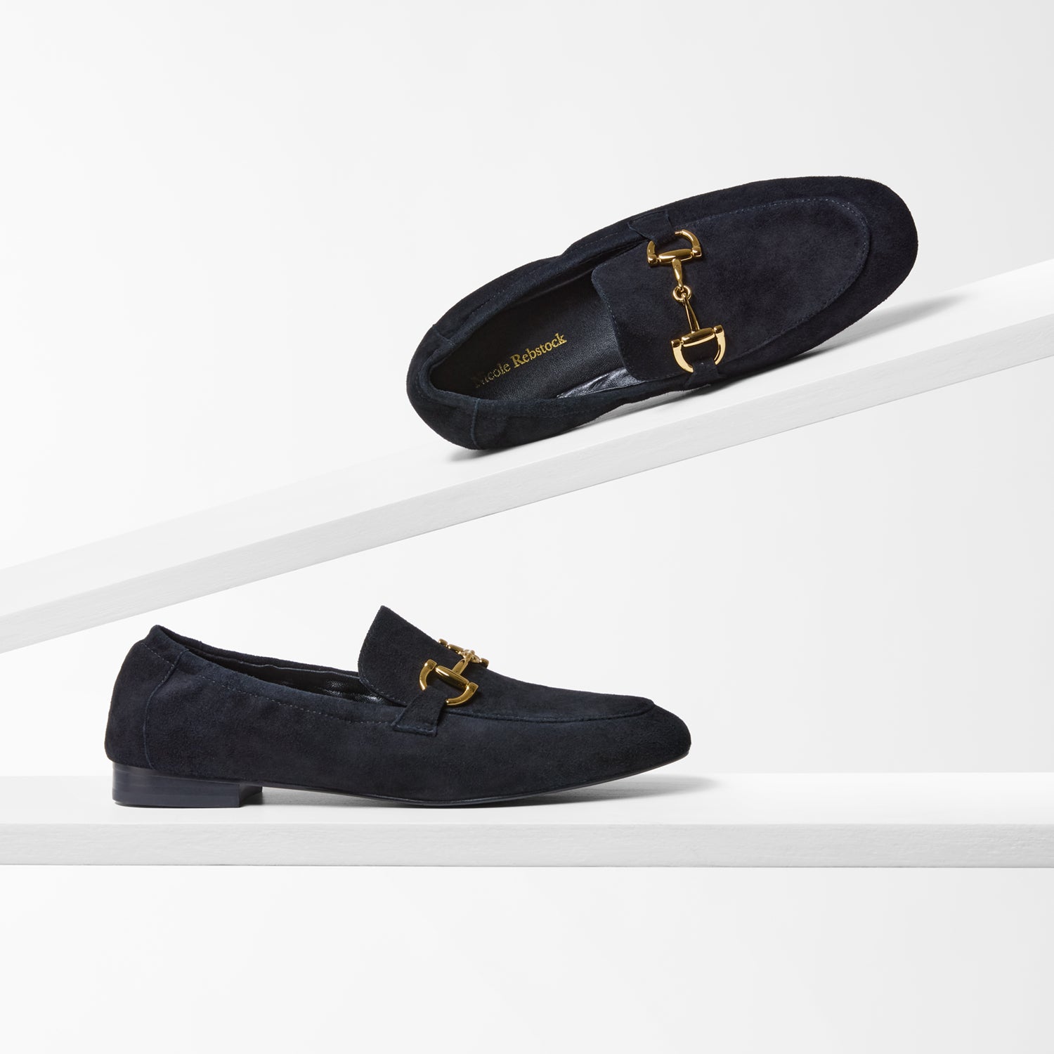 Pair of black loafers with gold buckles on a white background by Nicole Rebstock