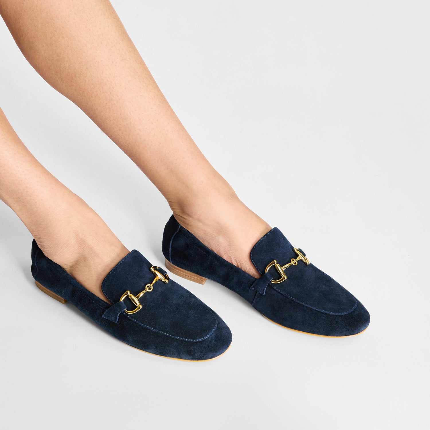 Navy loafers with gold buckles worn by a person on a light gray background. 2cm heel