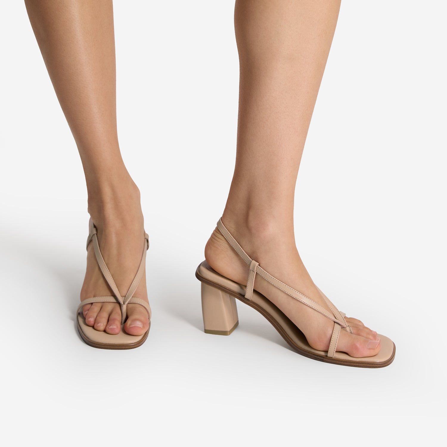 Light tan high-heeled sandals worn by a person on a white background. Square toe and small platform.