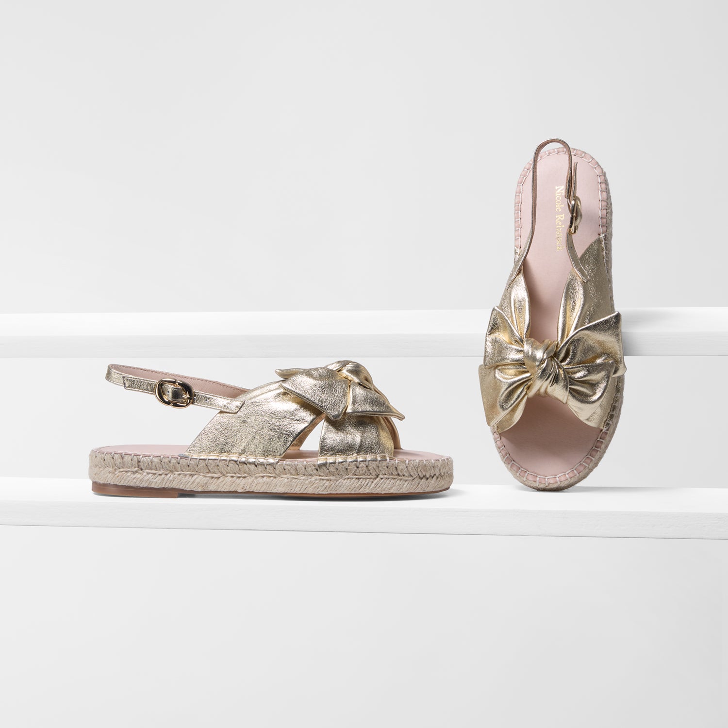 Pair of gold sandals with bow details on a white background