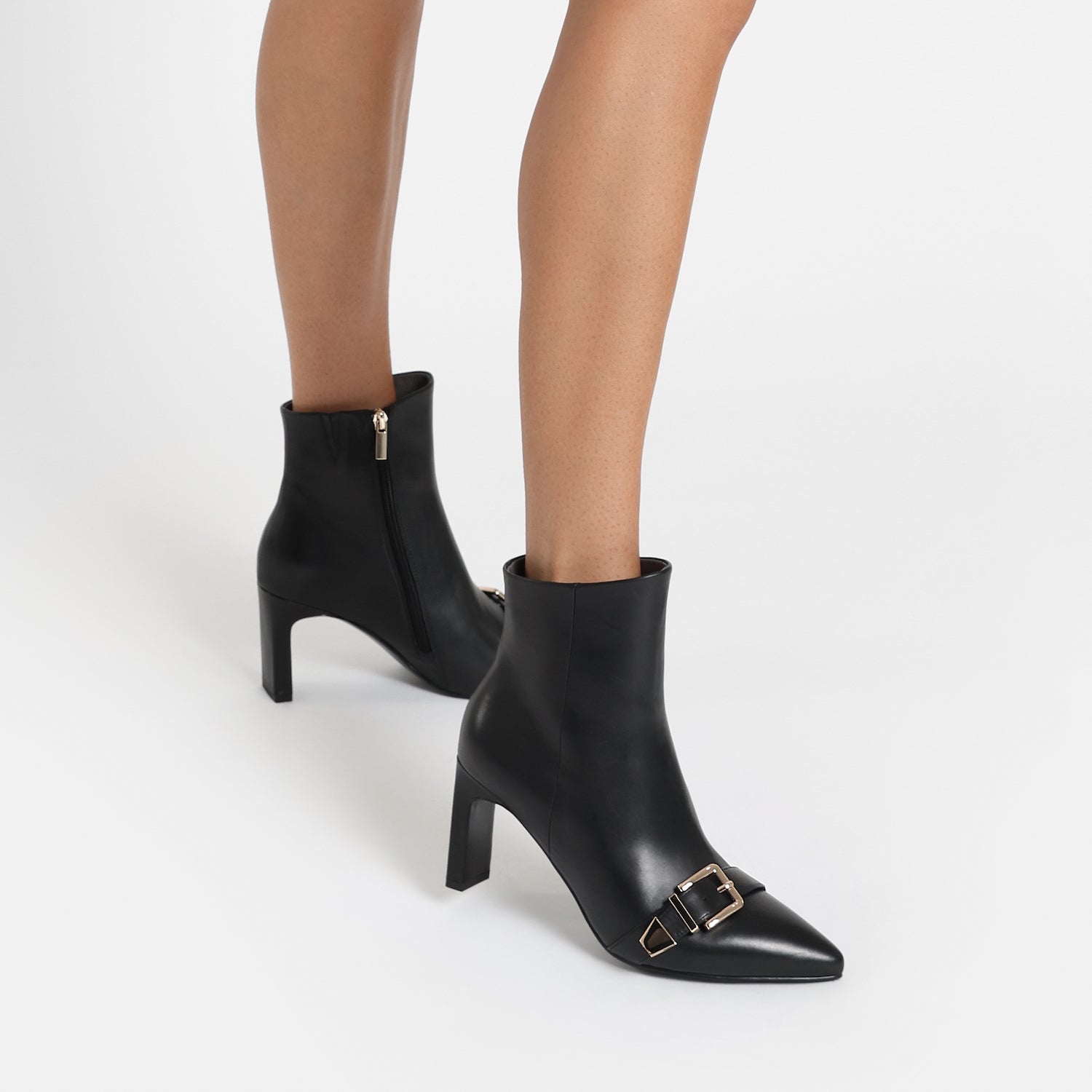 Close up of black Rome Ankle Boot. Featuring gold buckle on toe.