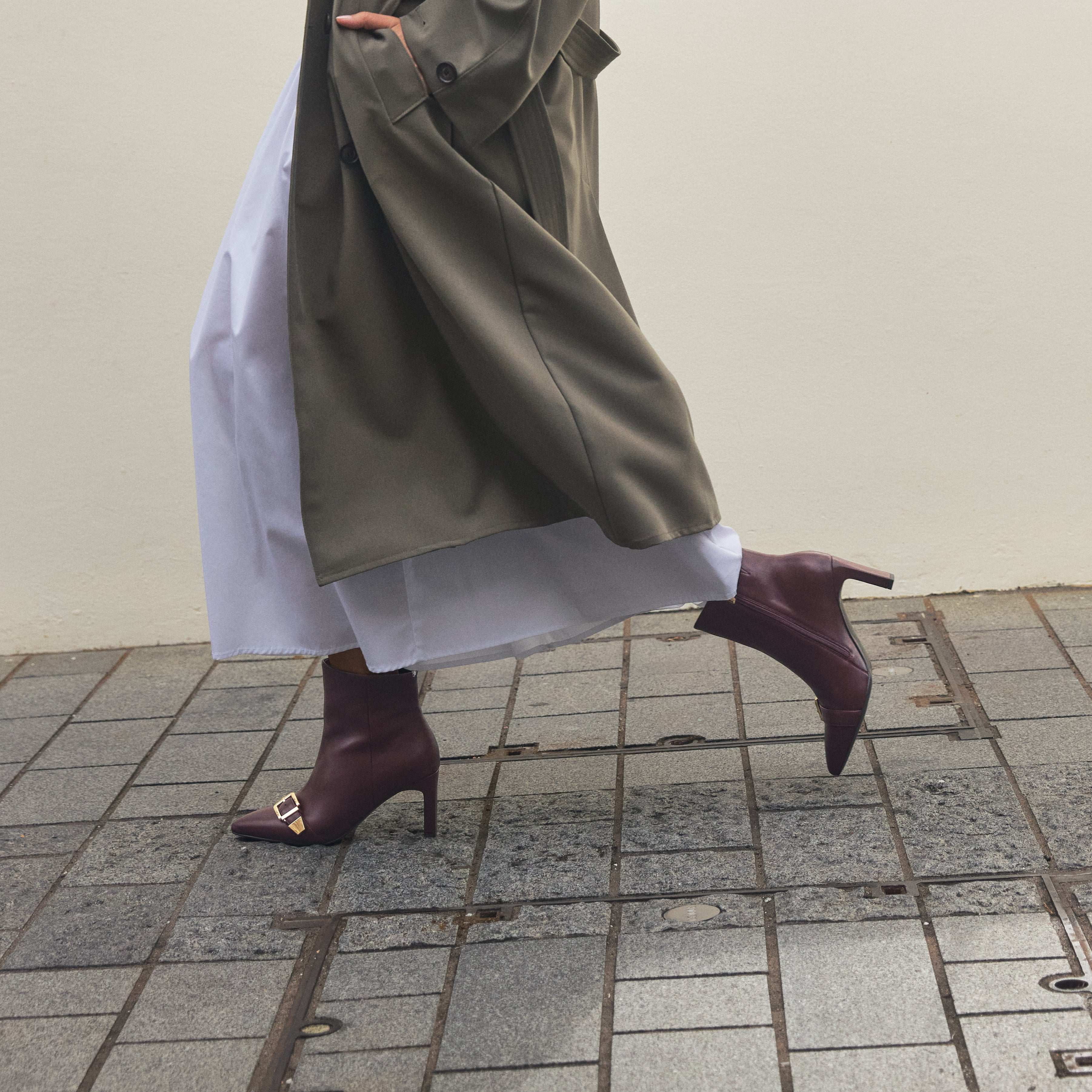 Close up on woman of Rome Ankle boot in Oxblood. The shoes have gold buckles and a slim block heel.