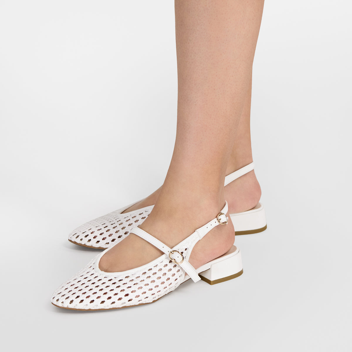 White perforated leather flat sandals with mary jane straps and low block heels, shown on a model's feet against a light gray studio background.
