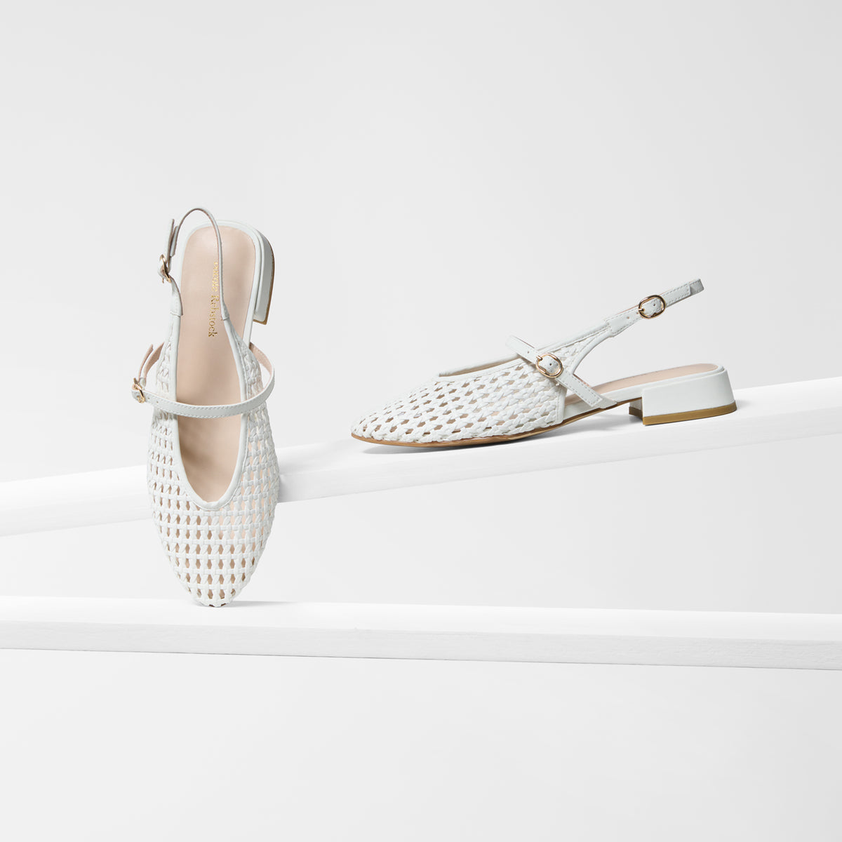 A pair of white woven slingback flats with low block heels, displayed on a clean white geometric platform against a white background.