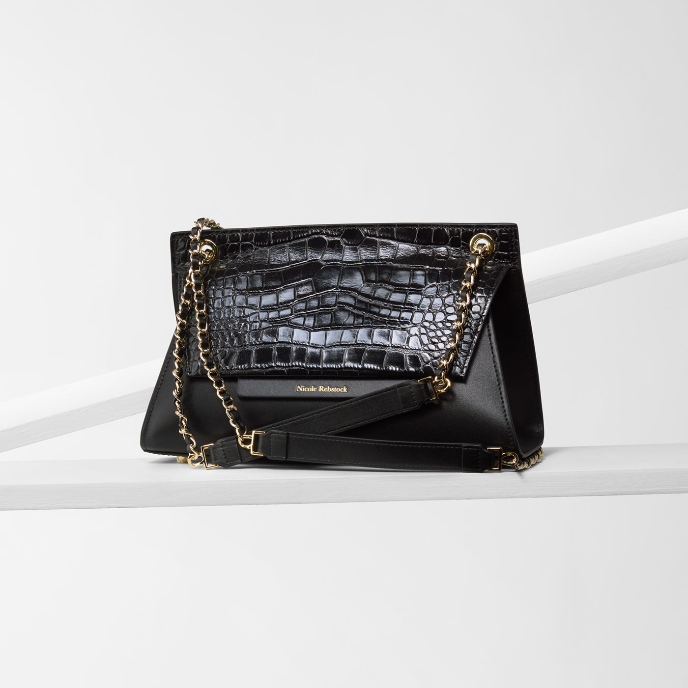 A black leather handbag with an embossed print and gold metal hardware, featuring a chain shoulder strap.