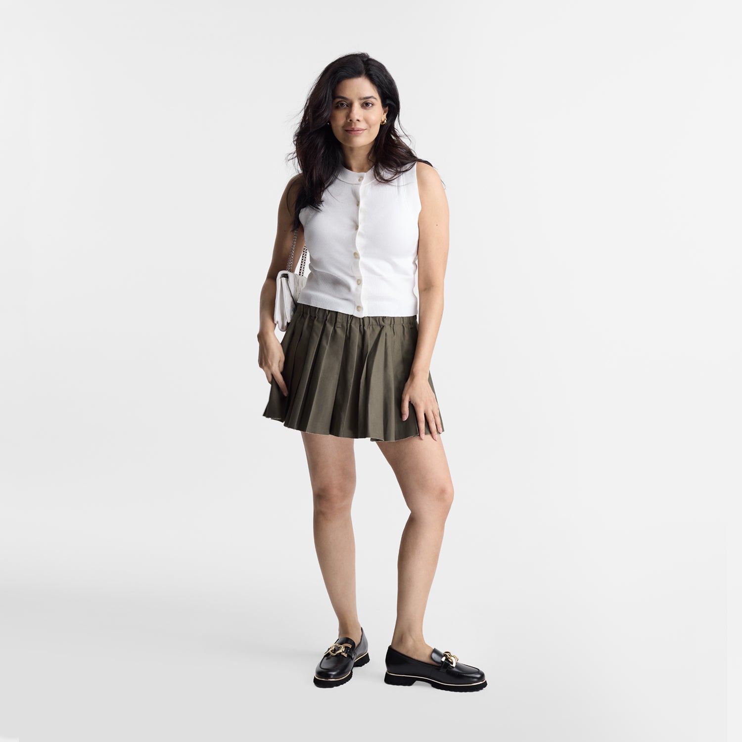 Woman wearing a white sleeveless top and pleated skirt with black Nicole Rebstock loafers on a white background