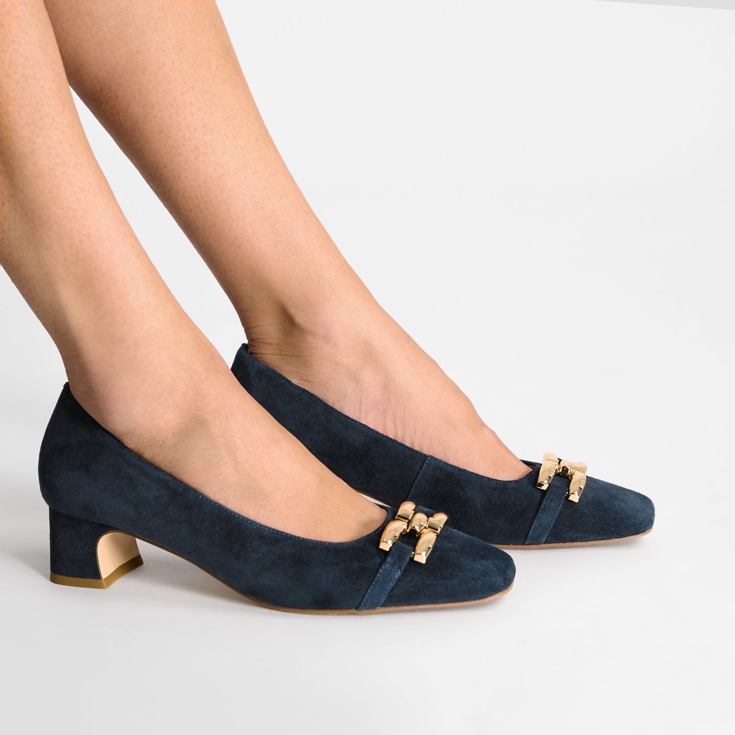 Navy blue high-heeled shoes with gold accents worn by a person on a light gray background