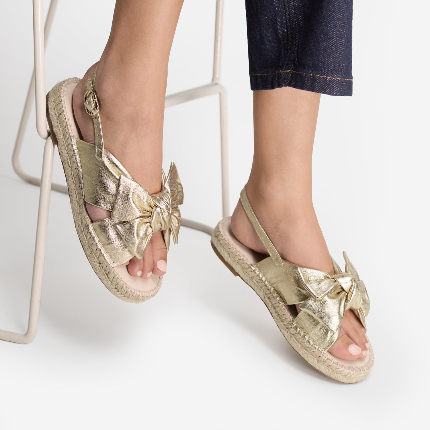 Champagne leather sandals with bow details worn by a person on a white background