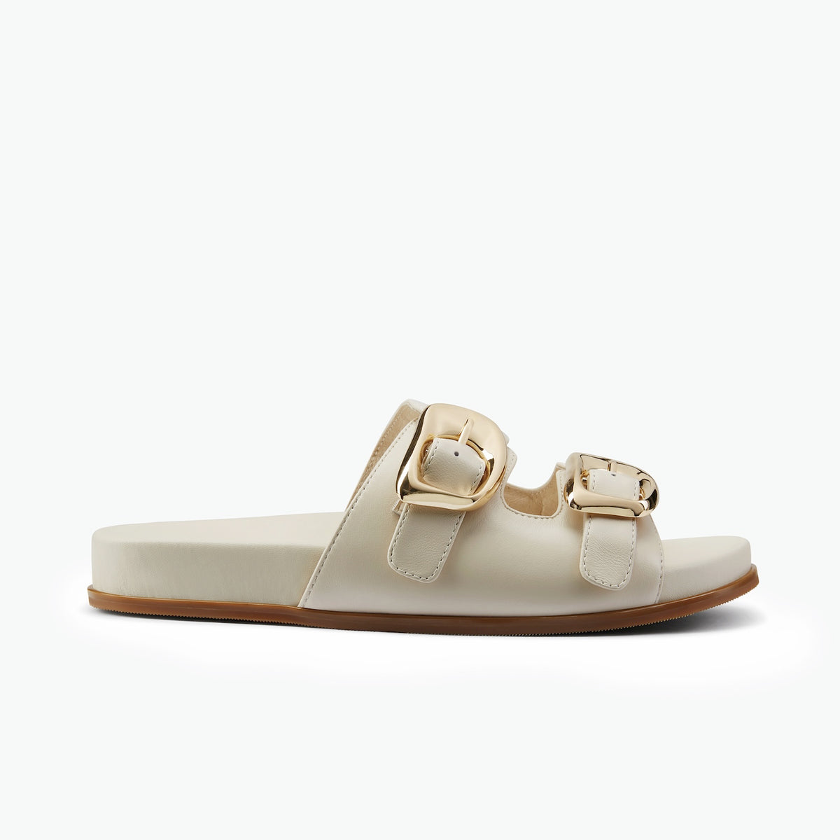 A single slide sandal in off-white faux leather with two wide straps featuring large gold-tone buckles, shown in profile against a clean white background.