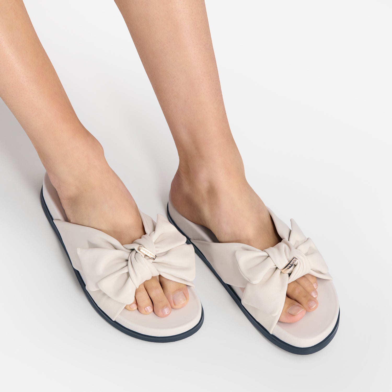 A pair of women's slide sandals with large bow details on the toes, shown being worn on a person's feet against a clean white background.