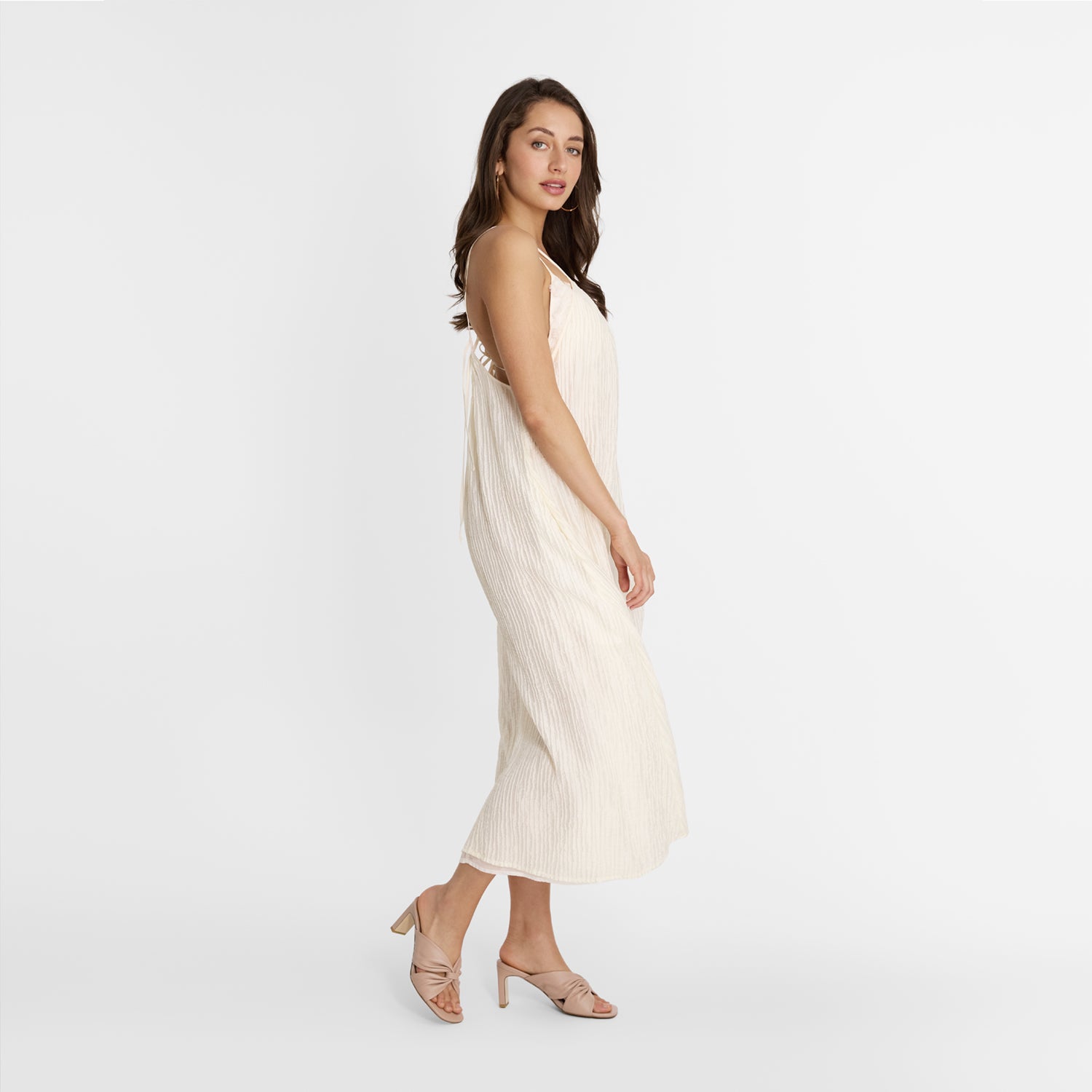 Woman wearing Nicole rebstock Mule heels and a white dress on a plain background