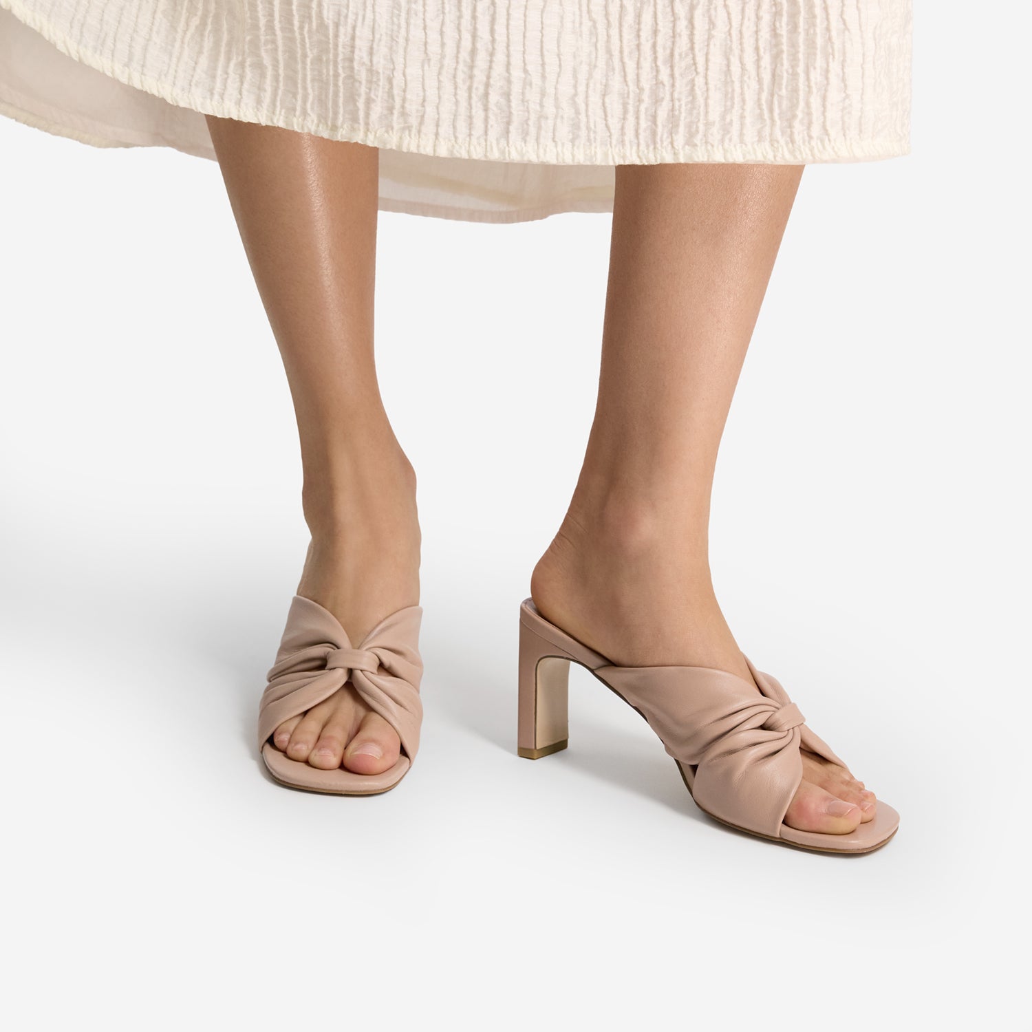 nude high-heeled sandals worn with a light-colored skirt on a white background