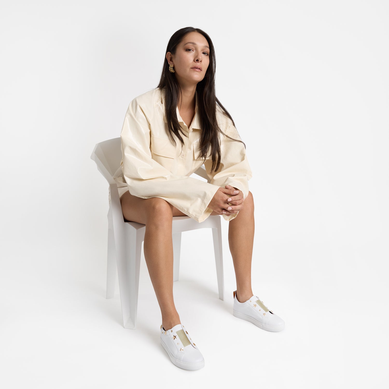 Felix white slip-on sneakers on sitting model with gold elastic and gold star studs.